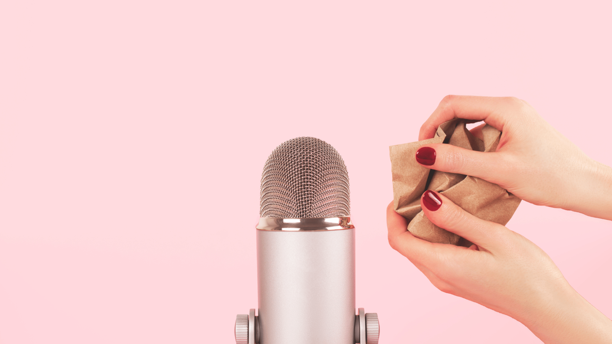 Manicured hands scrunching up some paper next to a silver microphone with a pink background