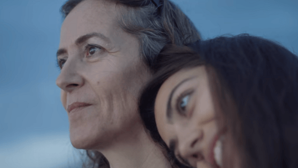 A close-up brand film still of a woman resting her head on another woman. They are both smiling