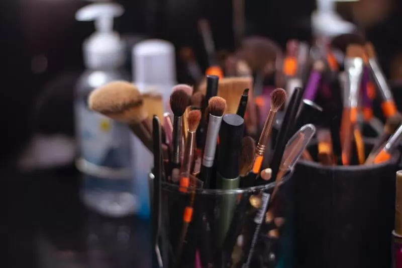A clear glass holds different sized and multi-coloured makeup brushes on the set of a video shoot.
