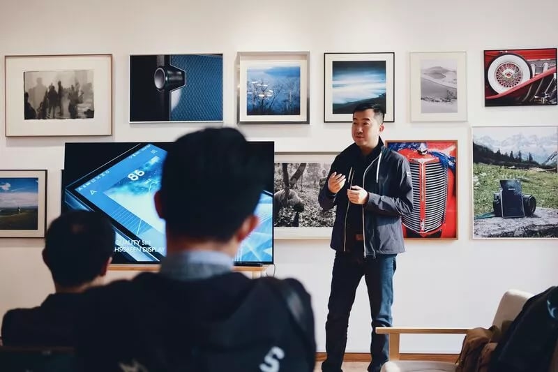 A man stands up in front of a class and seems to be explaining a concept to them