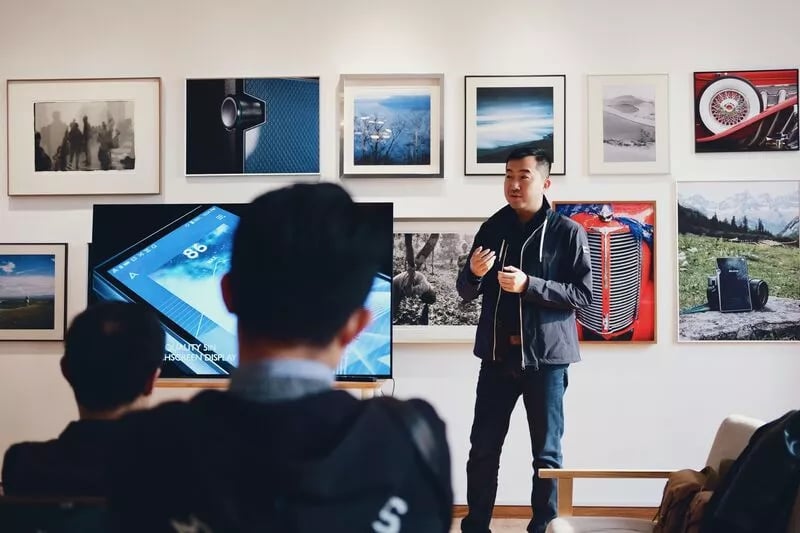 A man stands up in front of a class and seems to be explaining a concept to them 