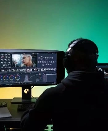 A man wearing headphones sits at a computer editing a video